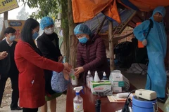 Bí thư Tỉnh ủy Hoàng Thị Thúy Lan (áo đỏ) dùng dung dịch sát khuẩn tại chốt kiểm soát số 1 lối vào chính của xã Sơn Lôi. (Ảnh: Hoàng Hùng/TTXVN)