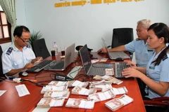 Cán bộ Hải quan cửa khẩu Mộc Bài kiểm tra số lượng tiền bath Thái Lan thu giữ. (Ảnh: Lê Đức Hoảnh/TTXVN)