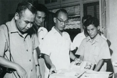 Nhà báo Bùi Đình Túy (người đeo kính) hướng dẫn phóng viên Nhật Bản Konishi xem các bộ ảnh triển lãm do TTXVN biên soạn, tháng 7/1964. (Nguồn: TTXVN)