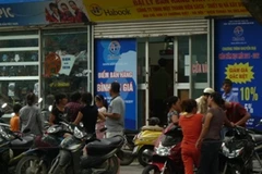 Các "cò sách giáo khoa" ngồi buôn chuyện với nhau trước cổng nhà sách. (Ảnh: Hồng Kiều/Vietnam+)