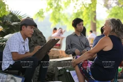 Du khách nước ngoài đang được các họa sỹ vẽ tranh ký họa bên Hồ Gươm. (Ảnh: Tất Sơn/Báo ảnh Việt Nam)