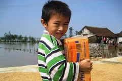 Niềm vui của em bé Can Lộc khi được nhận mỳ tôm cứu trợ. (Ảnh: Sơn Bách)