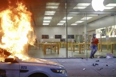 Một người chạy khỏi Apple Store tại Philadelphia trong khi một chiếc xe cảnh sát đỗ phía trước cửa hàng bị đốt cháy, ngày 30/5/2020. (Nguồn: AP)