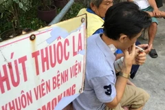 Vô tư nhả khói trong khuôn viên bệnh viện dù bảng cấm hút thuốc ngay bên cạnh. (Ảnh: Đinh Hằng/TTXVN)
