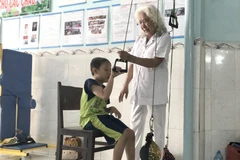 Bà Nguyễn Ngọc Điểu tập luyện phục hồi chức năng vận động cho bé Phan Thanh Phong. (Ảnh: Lê Thúy Hằng/TTXVN)
