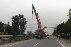 Xe cẩu đến ứng cứu kéo chiếc xe tải ra khỏi hộ lan giữa đường sắt và đường bộ. (Ảnh: PV/Vietnam+)