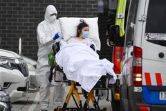 Nhân viên y tế chuyển bệnh nhân COVID-19 lên xe cứu thương tại thành phố Melbourne, Australia. (Ảnh: AFP/TTXVN) 