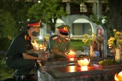 Thắp nến lên các phần mộ liệt sỹ. (Ảnh: Xuân Tư/TTXVN) 