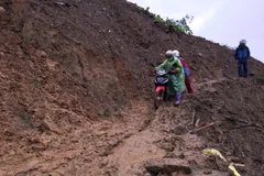 Các giáo viên điểm trường mầm non Hoa Đào, xã Suối Bâu, huyện Phù Yên dắt xe máy qua điểm sạt lở. (Ảnh: Hữu Quyết/TTXVN)