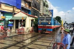 Tàu hỏa chạy qua một đường ngang có nhân viên đường sắt chốt trực tại gác chắn. (Ảnh: Việt Hùng/Vietnam+)