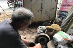 Người thợ rèn Đa Sỹ mài những lưỡi dao qua máy để làm sáng và loại bỏ những mạt sắt bám vào dao trong quá trình nung. (Nguồn: Vietnam+)