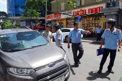 Lực lượng chức năng xử lý các ô tô đậu lấn chiếm lề đường. (Ảnh: Mạnh Linh/TTXVN)