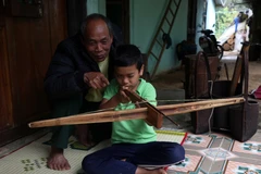 Già làng Hồ Xuân Thiện hướng dẫn cháu nội cách sử dụng nỏ. (Ảnh: Đỗ Trưởng/TTXVN)