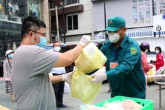 Lực lượng chức năng phường 12, quận 3 hỗ trợ người dân mua hàng hóa, thực phẩm các loại và trứng tại điểm xe bán hàng lưu động của Sở Công thương thành phố. (Ảnh: Thanh Vũ/TTXVN)