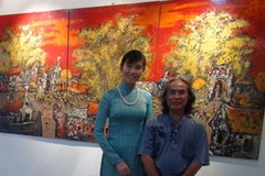 Họa sỹ Lương Khánh Toàn đứng bên một bức tranh sơn mài trưng bày tại triển lãm. (Ảnh: Ngọc Tiến/Vietnam+)