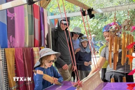 Du khách quốc tế thích thú khi được trải nghiệm quá trình dệt thổ cẩm của người dân tộc Thái. (Ảnh: Hoa Mai/TTXVN)