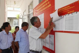 Người dân xem danh sách cử tri được niêm yết tại điểm bỏ phiếu. (Ảnh: Nhựt An/TTXVN)