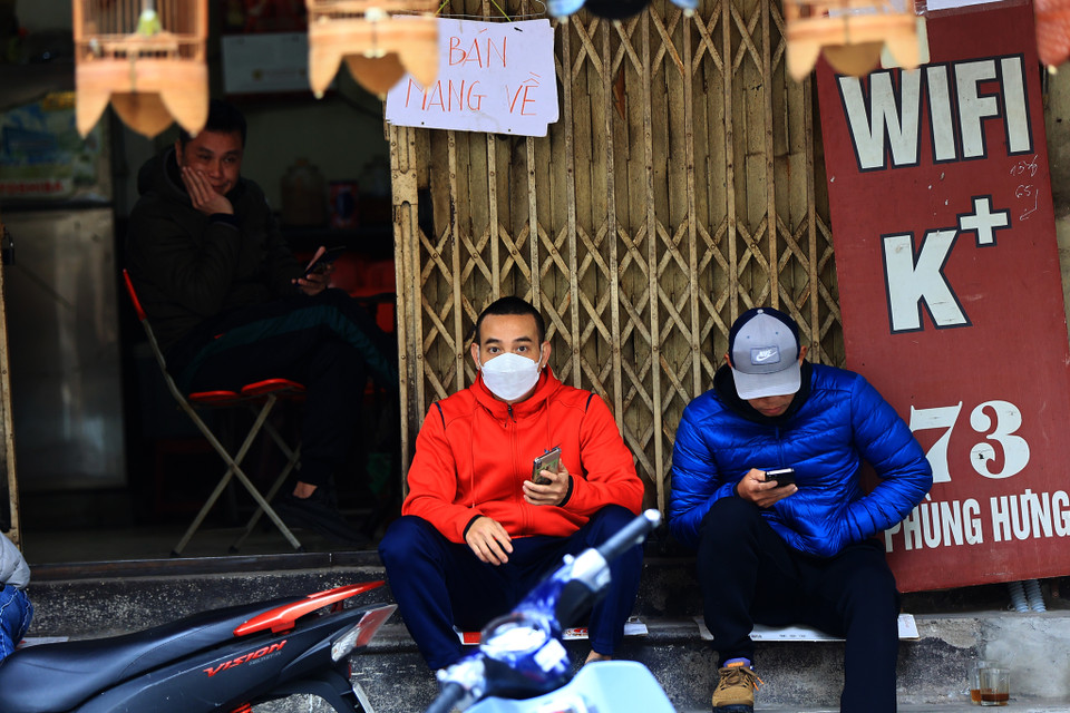 Quán cà phê này vừa treo biển ‘Bán mang về’ nhưng thực chất vẫn phục vụ khách tại cửa hàng. Các vị ‘thượng đế’ chấp nhận ngồi trên bậc thềm của cửa hàng để uống nước. (Ảnh: Hoài Nam/Vietnam+)