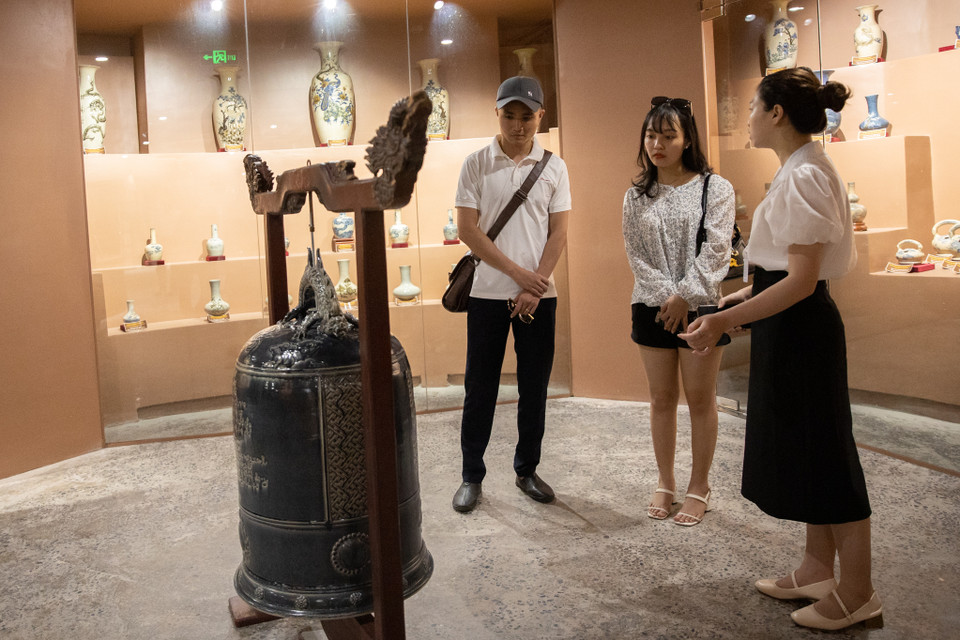 Ở mỗi tầng đều có hướng dẫn viên giúp du khách tìm hiểu về thông tin của từng đồ vật được bày trí trong không gian gốm. Trong ảnh, du khách đang được giới thiệu về chiếc chuông bằng gốm- mô phỏng từ chiếc chuông đồng của đình làng Bát Tràng. (Ảnh: Hoài Nam/Vietnam+)
