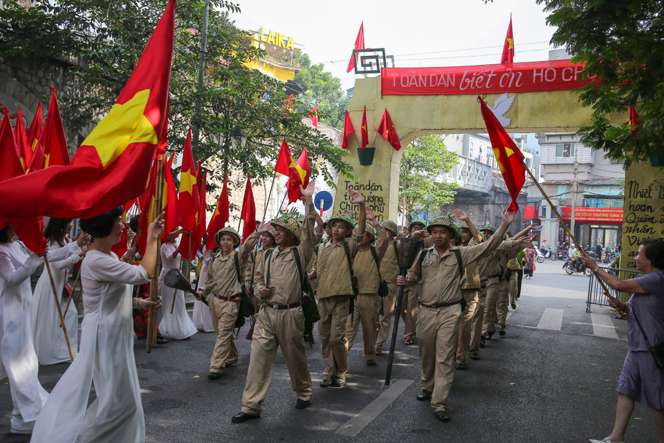 Hàng trăm người dân ăn mặc theo phong cách người Hà Nội xưa, mang theo cờ đỏ sao vàng, hoa tươi đứng hai bên đường chờ đón bộ đội từ chiến khu Việt Bắc về tiếp quản Thủ đô. (Ảnh: Vietnam+)