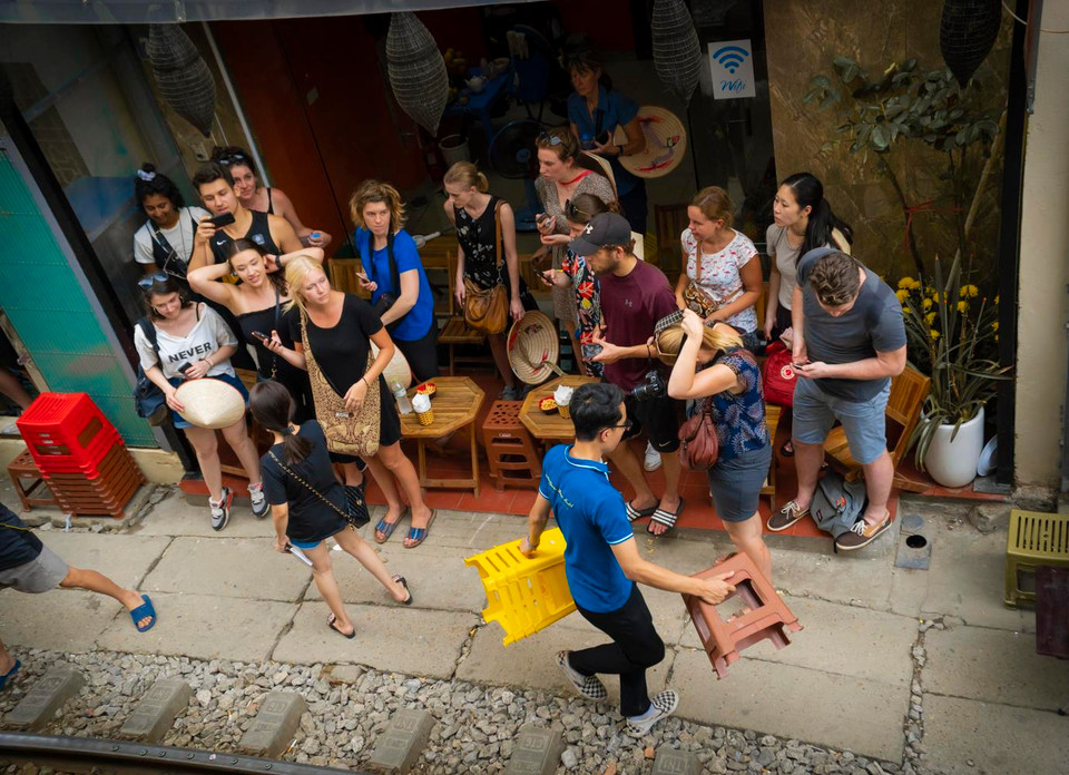 Mỗi khi có đoàn tàu sắp chạy qua trước vài phút, các chủ quán càphê sẽ hớt hải 'chạy đôn chạy đáo' thu dọn bàn ghế, nhắc nhở khách sẵn sàng tinh thần để 'né' tàu. (Ảnh: Minh Hiếu/Vietnam+)