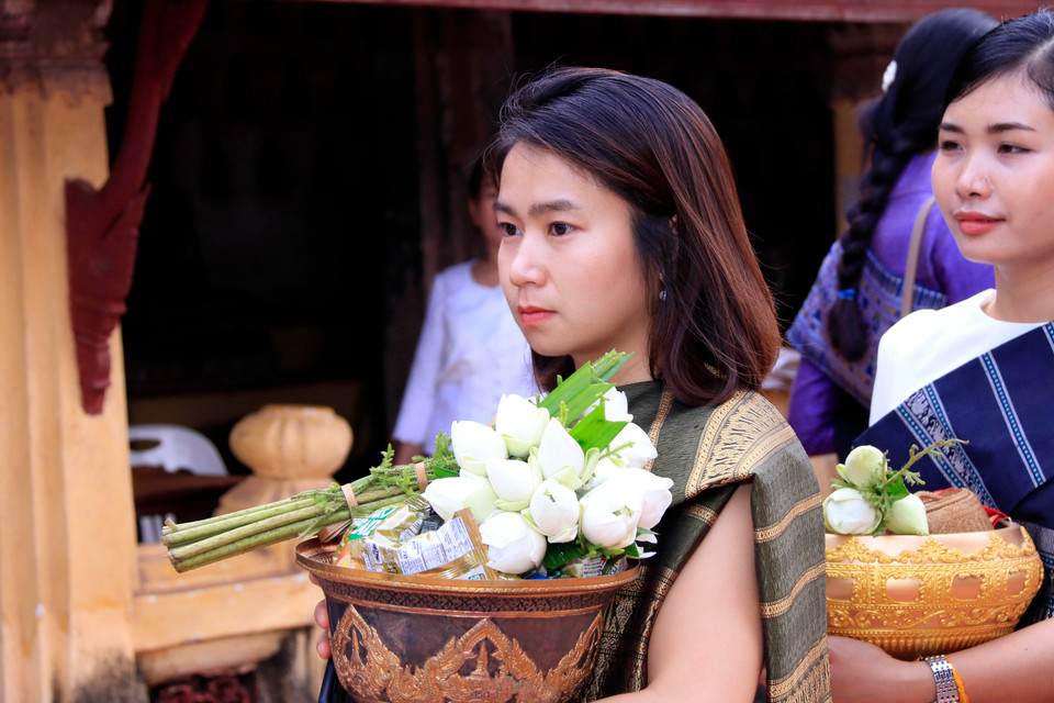 Một thiếu nữ Lào trong trang phục truyền thống đang xếp hàng chờ tới lượt vào thực hiện nghi thức Xaybath (Cúng dường) ở chùa Sisaketh, một ngôi chùa lớn ở thủ đô Viêng Chăn. (Ảnh: Phạm Kiên/TTXVN)