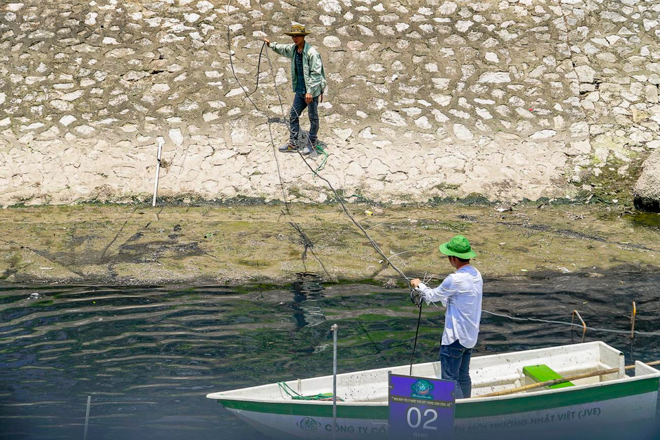 Hai công nhân đang chuẩn bị dụng cụ lấy mẫu nước sông để nghiên cứu. (Ảnh: PV/Vietnam+)