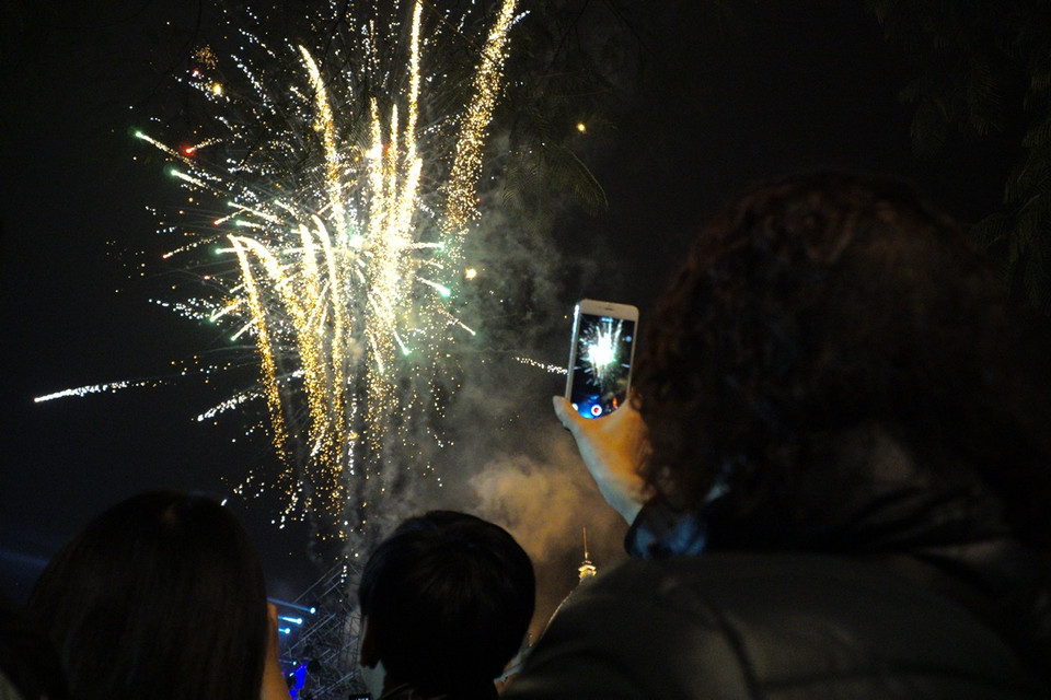 Người dân đang ghi hình lại màn trình diễn pháo bông nghệ thuật từ Quảng trường Tháng Tám rực rỡ và đầy sắc màu. (Ảnh: Minh Hiếu/Vietnam+)
