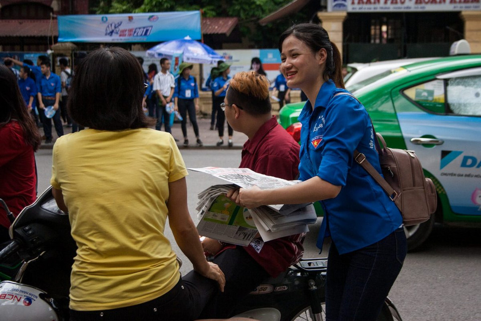 Tại điểm thi trường Trần Phú-Hoàn Kiếm, sinh viên tình nguyện phát báo cho phụ huynh trong lúc các thí sinh làm thủ tục. (Ảnh: Doãn Đức/Vietnam+)
