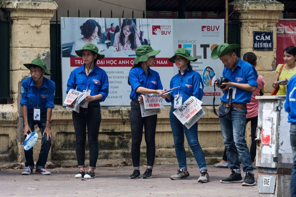 Tại điểm thi trường Trần Phú-Hoàn Kiếm, sinh viên tình nguyện phát báo cho phụ huynh trong lúc các thí sinh làm thủ tục. (Ảnh: Doãn Đức/Vietnam+)
