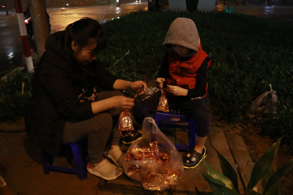 Hai mẹ con chị Linh đang ngồi thắt từng túi muối lộc, chị cho biết sẽ về nhà sớm nếu trời tiếp tục mưa. (Ảnh: Minh Hiếu/Vietnam+)