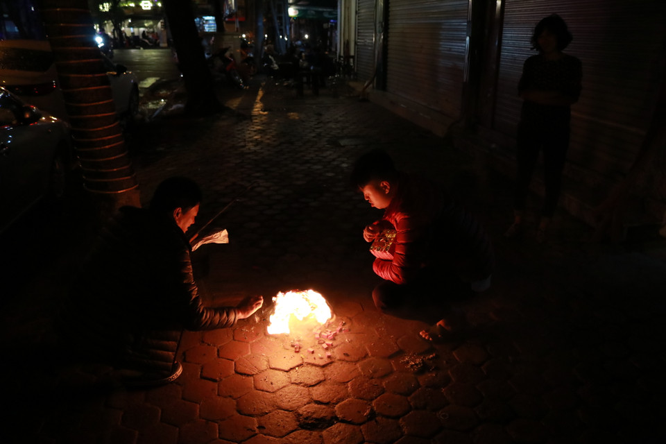 Nhiều gia đình vẫn hoá vàng cúng giao thừa dưới trời mưa. (Ảnh: Minh Hiếu/Vietnam+)