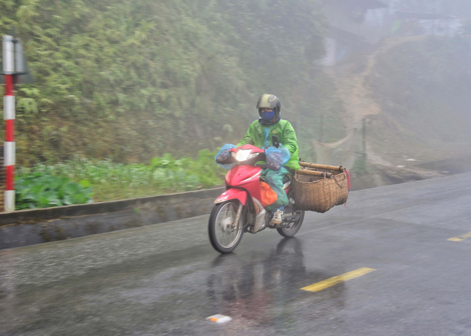 Người dân đi xe máy vận chuyển hàng hóa trong sương sớm, giá lạnh trên đỉnh đèo Pha Đin. (Ảnh: Xuân Tiến/TTXVN)
