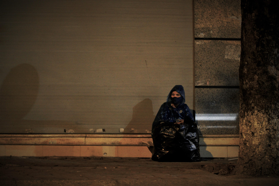 Một cụ già đang co ro vệ đường với chiếc áo mưa tránh cái lạnh đầu mùa. (Ảnh: Minh Hiếu/Vietnam+)