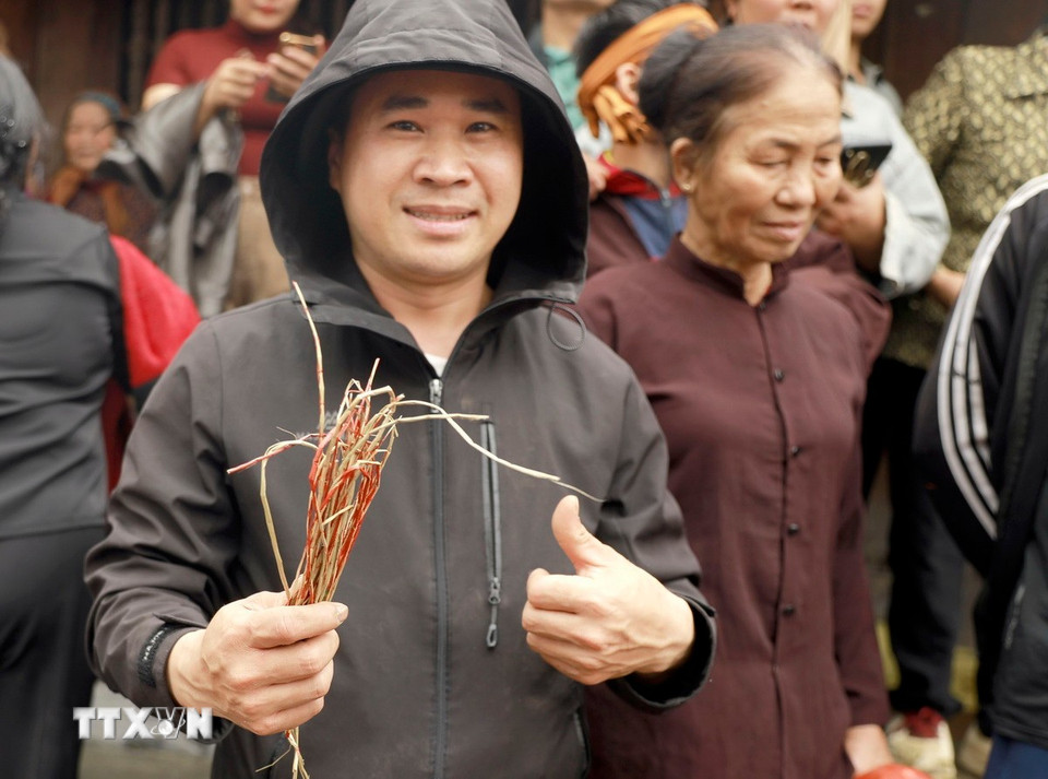 Niềm vui của người dân khi cầm trên tay mảnh chiếu thánh sau nghi thức xé chiếu cầu may tại Đình Cả Phù Liễn. (Ảnh: Hoàng Hùng/TTXVN)