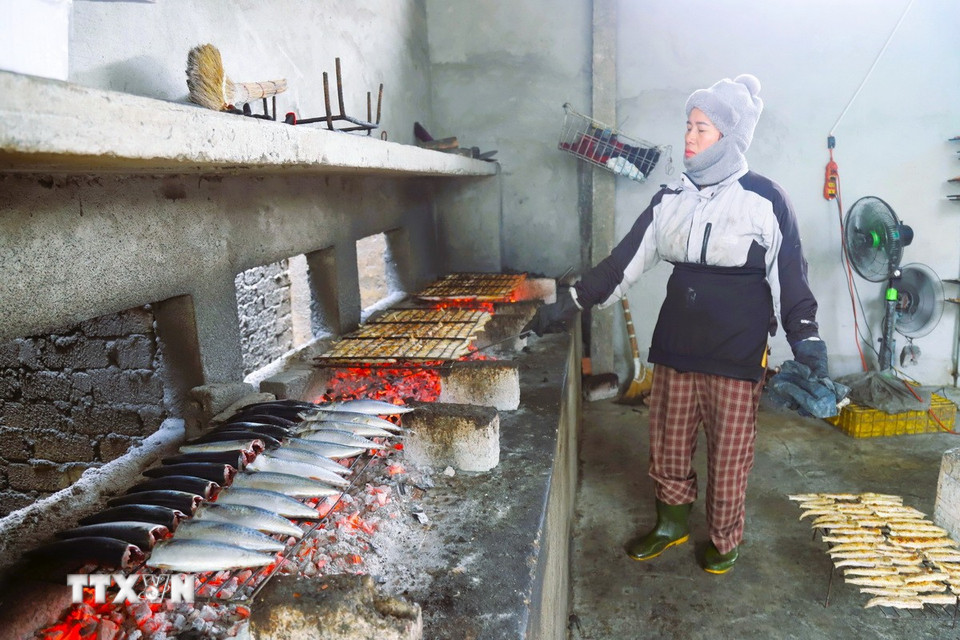 Người trực tiếp nướng cá phải luôn túc trực bên lò nướng để khều than, tiếp than giữ cho nhịp lửa than luôn đượm và dàn đều diện tích, giúp cá mau chín, chín đều.(Ảnh: Xuân Tiến/TTXVN)