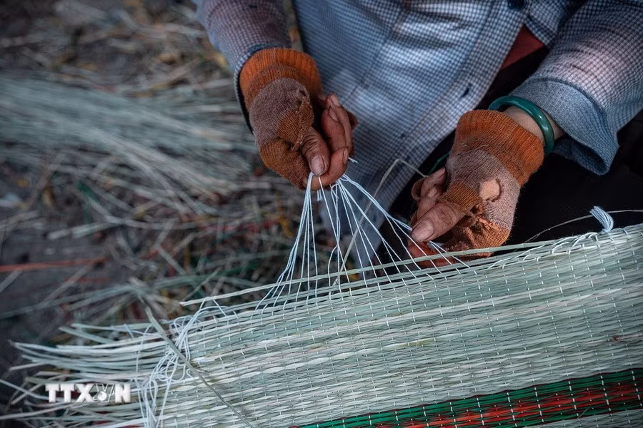 Tỉ mỉ buộc những sợi dây dù trắng quanh mép chiếu. (Ảnh: Khánh Hòa/TTXVN)