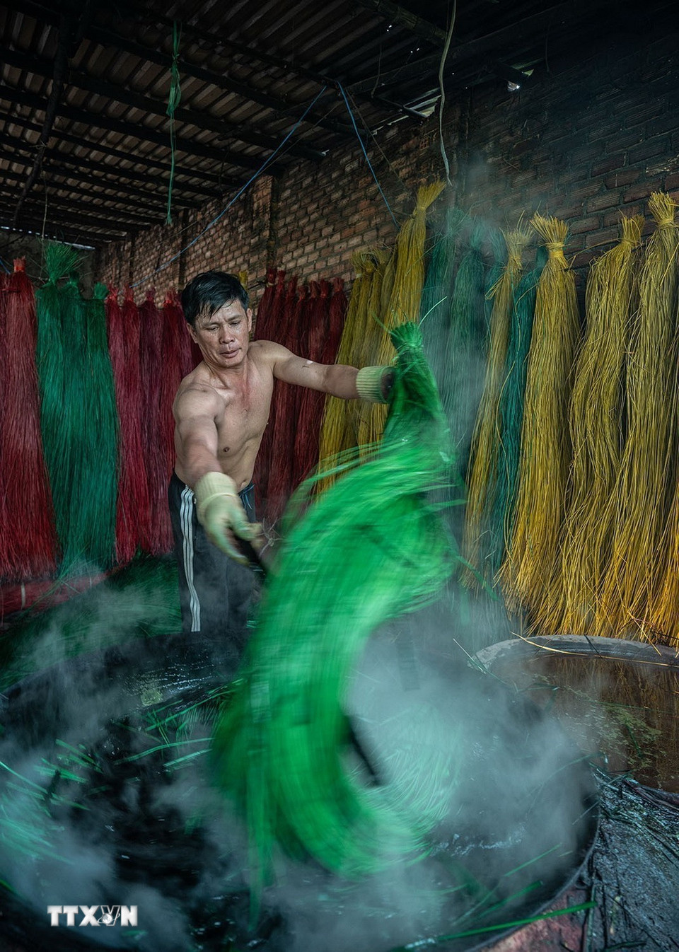 Sợi cói phải được nhúng đều vào nước nhuộm đang đun sôi để giữ được màu tươi lâu hơn. (Ảnh: Khánh Hòa/TTXVN)