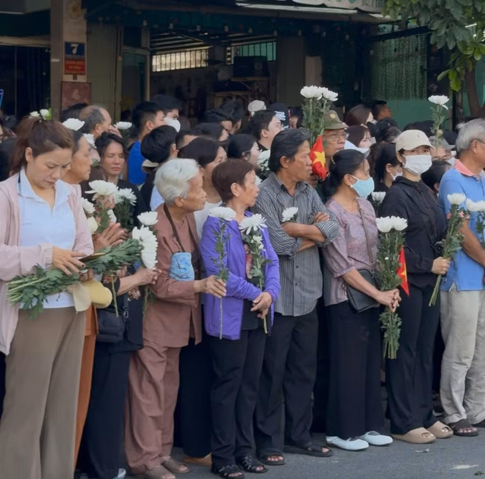 Dọc đường Trường Sơn, người dân đứng kín vỉa hè, cầm hoa trắng, cúi đầu khi đoàn xe đi qua. (Ảnh: PV/Vietnam+)