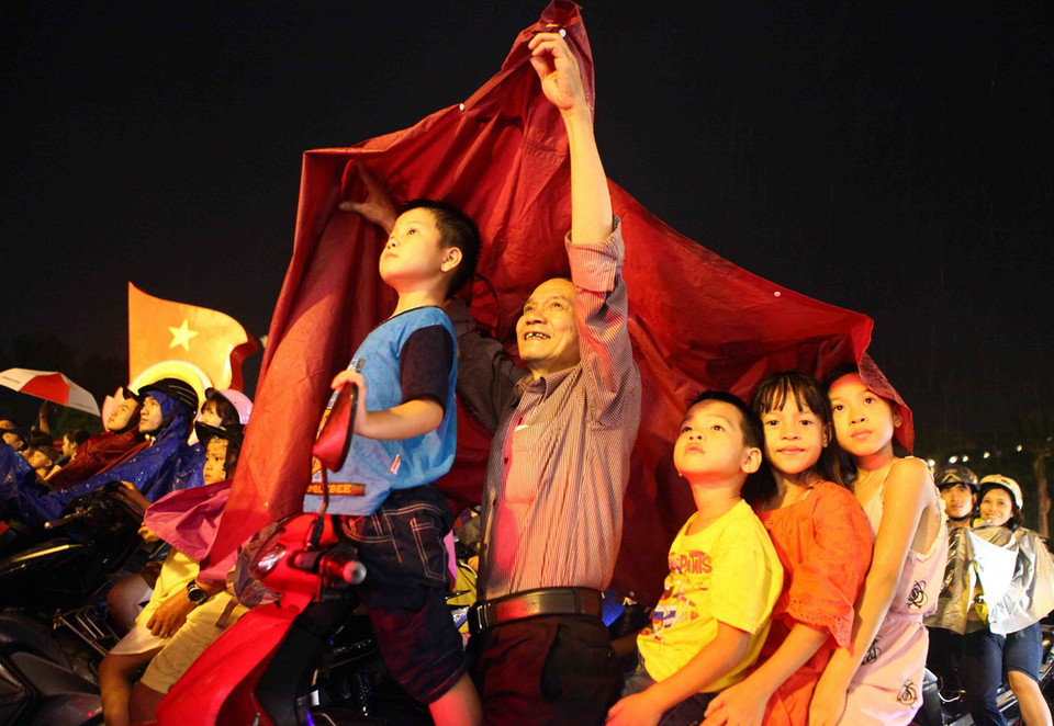 Người dân đứng tại Quảng trường Cánh mạng Tháng Tám xem bắn pháo hoa khu vực Hồ Hoàn Kiếm (Hà Nội). (Ảnh: Quý Trung/TTXVN)