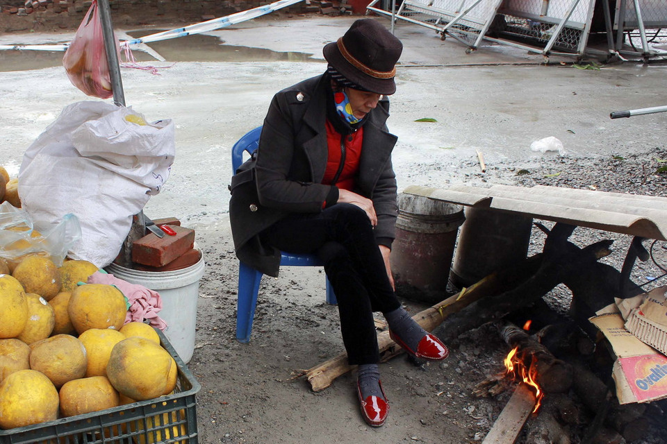 Những người bán hàng phải đốt lửa để sưởi ấm khi nhiệt độ ngoài trời xuống thấp. (Ảnh: Phạm Thảo/TTXVN) 