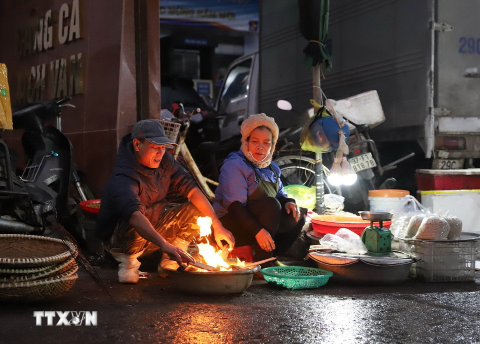 Người dân, tiểu thương đi chợ sớm đốt lửa để sưởi ấm trong thời gian chờ đợi tàu, thuyền cập cảng Lạch Vạn. (Ảnh: Xuân Tiến/TTXVN)