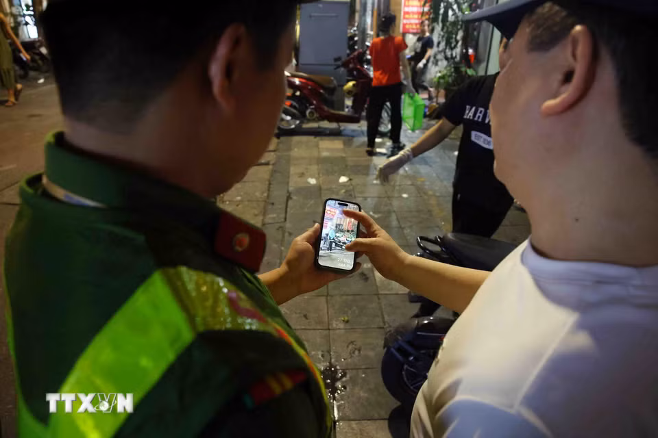 Cán bộ, chiến sĩ Công an phường Hoàn Kiếm cung cấp hình ảnh chứng minh vi phạm trật tự đô thị cho chủ cơ sở kinh doanh tại phố Nguyễn Siêu. (Ảnh: Phạm Kiên/TTXVN)