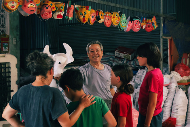 Ông Đông hào hứng chia sẻ cách làm mặt nạ bằng giấy bồi cho du khách nhí nước ngoài. (Ảnh: Hoài Nam/Vietnam+) vnp_11.jpg