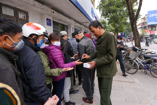 Bảo vệ liên tục đi phát số thứ tự cho người dân đến xếp hàng mua. (Ảnh: Minh Sơn/Vietnam+) Xếp hàng cả tiếng chờ mua 5 chiếc khẩu trang kháng khuẩn ở Hà Nội ảnh 6