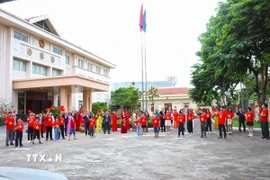 Cán bộ, nhân viên Đại sứ quán Việt Nam tại Lào giơ cao lá cờ đỏ sao vàng hướng về Tổ quốc. (Ảnh: Xuân Tú/TTXVN)