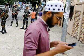 Một người dân sử dụng điện thoại bên cạnh lực lượng an ninh Sri Lanka đứng gác trên đường phố. (Nguồn: ndtv.com)