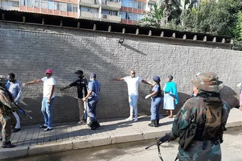 Lực lượng chức năng Nam Phi yêu cầu người dân thực hiện việc giãn cách xã hội khi xếp hàng mua thực phẩm thiết yếu. (Ảnh: Phi Hùng/TTXVN) 