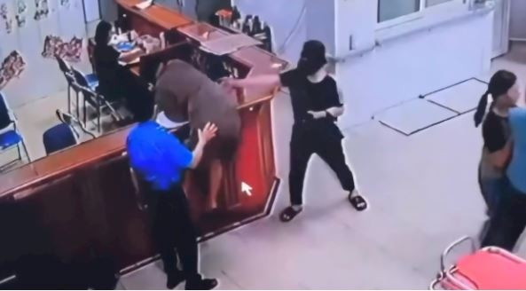 Người đàn ông chồm lên quầy làm thủ tục hành hung nhân viên bệnh viện. (Nguồn: Ảnh chụp màn hình)