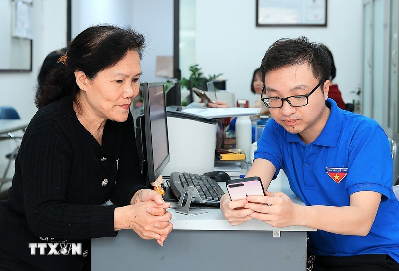 Đoàn viên thanh niên phường Hàng Bồ (quận Hoàn Kiếm, thành phố Hà Nội) hỗ trợ người dân thực hiện thủ tục hành chính công trên thiết bị điện thoại thông minh. (Ảnh: Phạm Hậu/TTXVN)